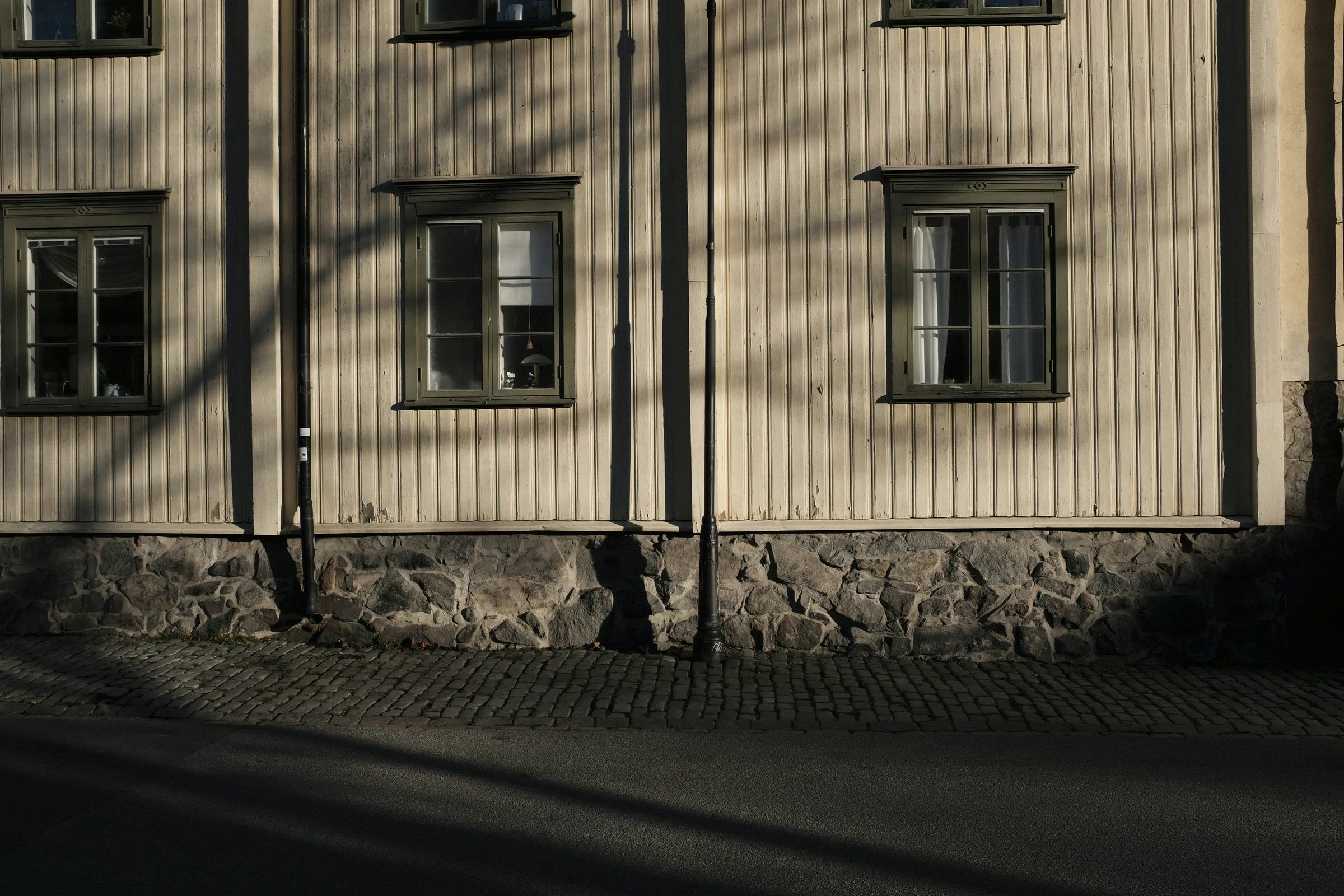 Ljus stående träpanel och spröjsade fönster på ett äldre hus med stengrund