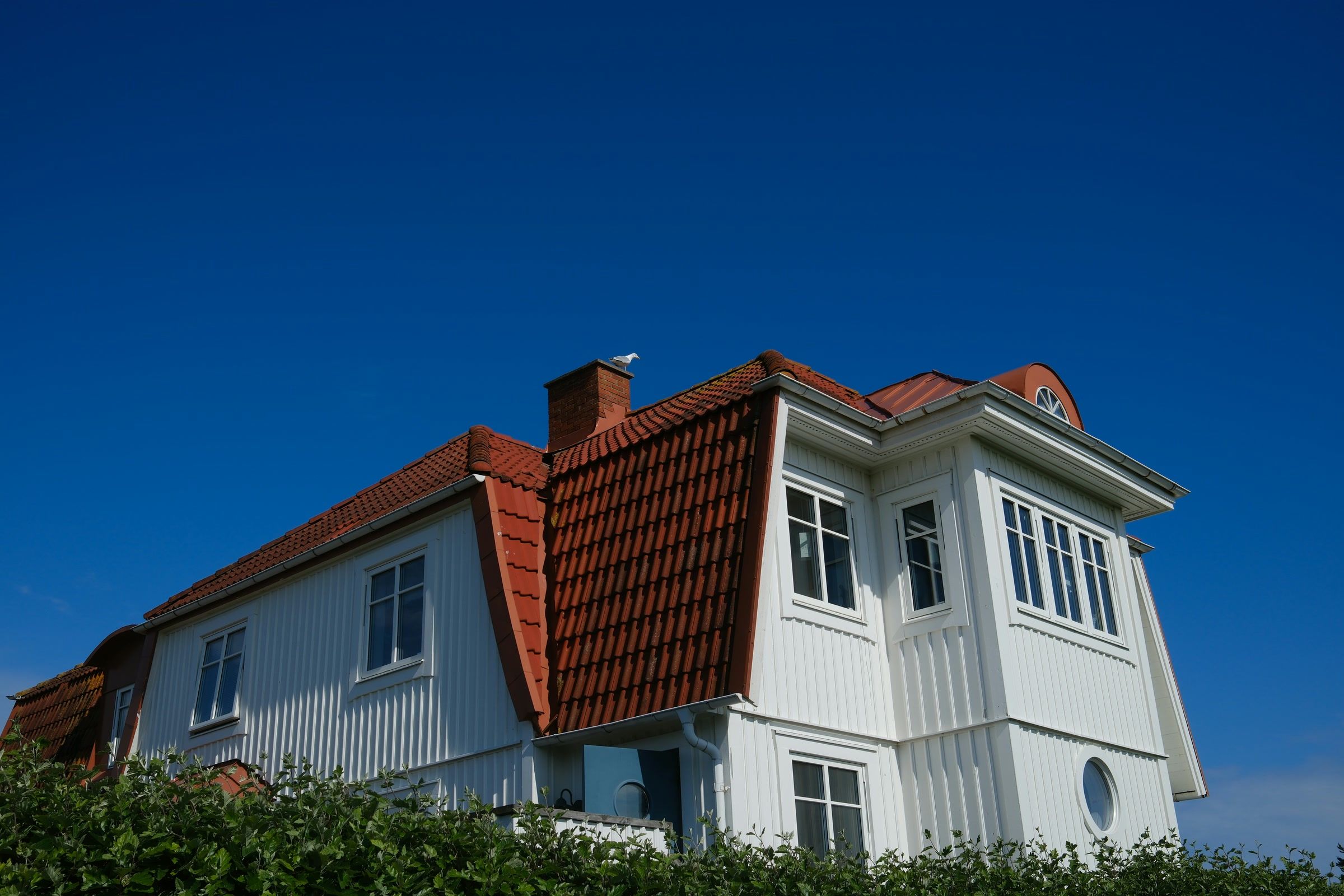 Vit trävilla med nylagt rött tegeltak och brutet tak mot blå himmel